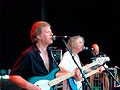 two men on stage singing and playing electric guitar