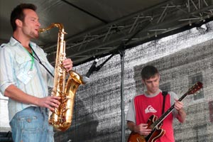 two men playing saxophone and electric guitar on stage